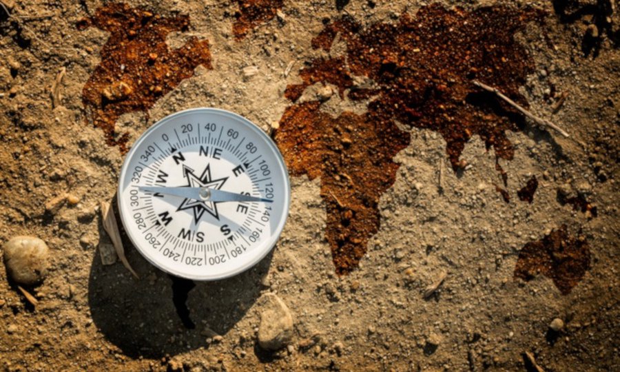 Compass on dry earth soil and world map