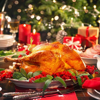 Christmas turkey dinner. Baked turkey garnished with red berries and sage leaves in front of Christmas tree and burning candles