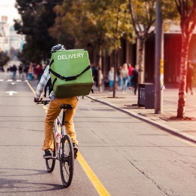 Delivery man food service courier on bicycle in town. Rear view of man riding a bicycle in the city street with green bag on back