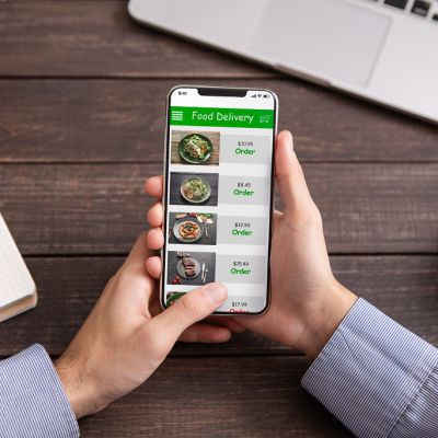 Takeaway service. Male hands touching smartphone screen with food delivery application, choosing meal for lunch, scrolling menu at workplace