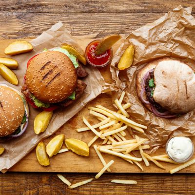 Fast food dish top view. Meat burger in craft paper, potato chips and wedges. Take away composition. French fries, hamburger, mayonnaise and ketchup sauces on wood. Menu or receipt background
