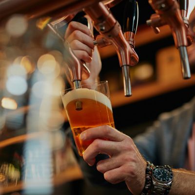 Tattooed caucasian barman pouring beer while standing in pub.