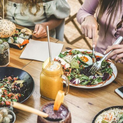 Hands view of young people eating brunch and drinking smoothies bowl with ecological straws in plastic free restaurant - Healthy lifestyle, food trends concept - Focus on top fork dish
