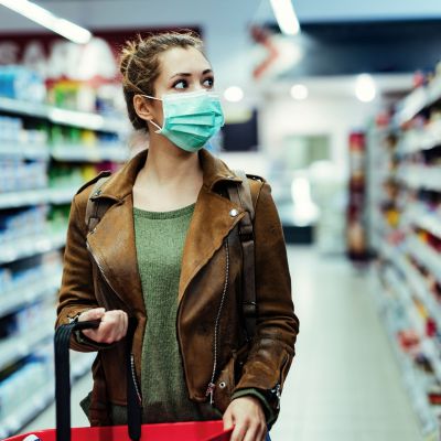 Young woman with face mask walking through grocery store during COVID-19 pandemic.