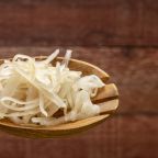 sauerkraut (fermented cabbage) on a wooden spoon against rustic barn wood background, probiotics concept - fermented food good for gut health, panoramic web banner
