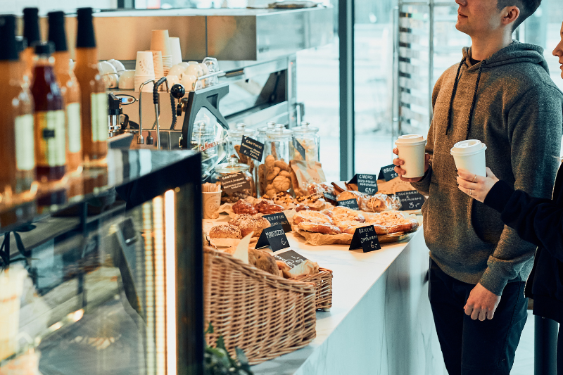 Two people holding coffee cups at a bakery counter with pastries.
