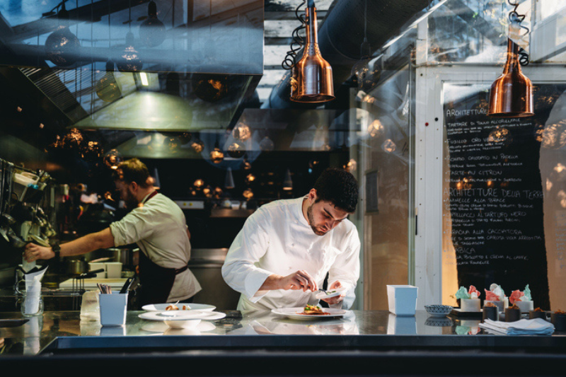 A chef is cooking in his restaurant's kitchen. Shot through the glass. High-end gourmet restaurant.