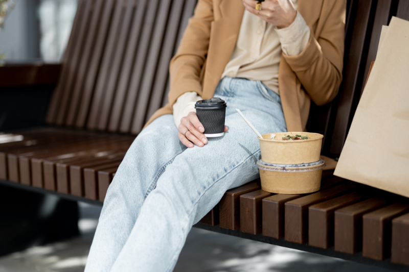 Person sitting on a bench with takeout food and coffee.