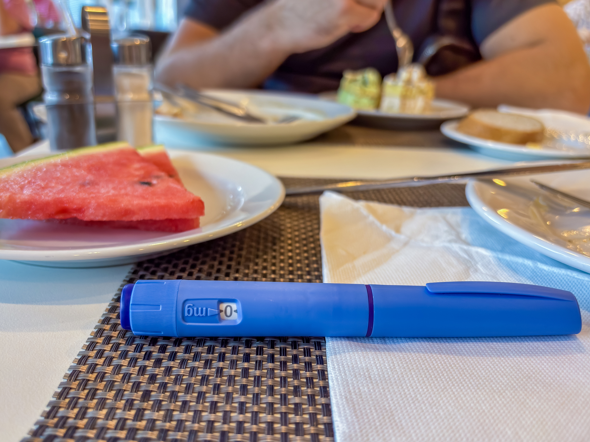 Ozempic semaglutide injection pen on restaurant table in front of person eating which is more hygienic toilet paper or bidet concept of diabetes medication, weight loss treatment, chronic disease