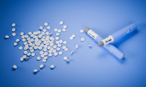 Weight loss pills available: Two dosing pens  for subcutaneous injection of antidiabetic medication or anti-obesity medication on a blue background besides a heap of GLP-1 pills.